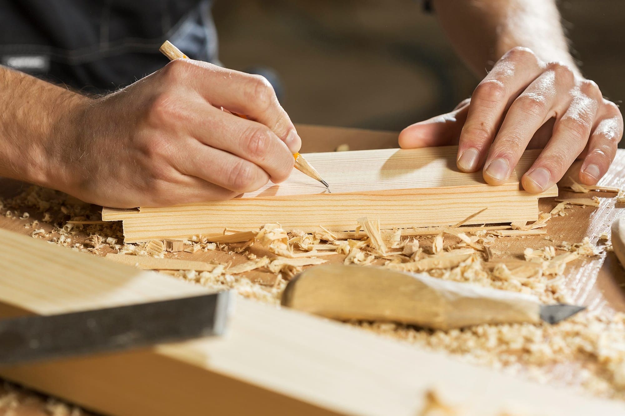A woodworker's hands marking a board on the bench among shavings